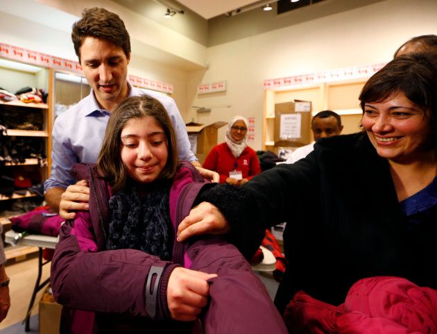 Prime Minister Justin Trudeau helps a young Syrian refugee try on a winter coat after she arrived with her family from Beirut at the Toronto Pearson International Airport in Mississauga, Ont., Dec. 11, 2015.