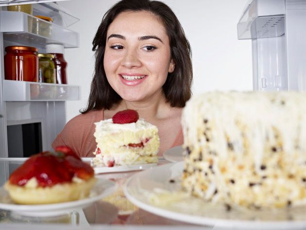 Woman looking at cake in through the fridge.