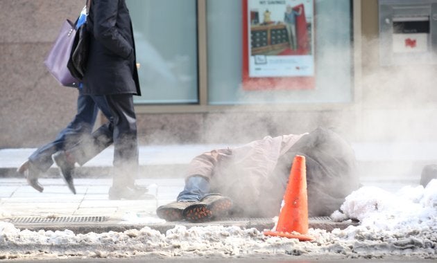 A homeless man sits on a city grate to keep himself warm wearing only a jacket in the frigid temperatures.