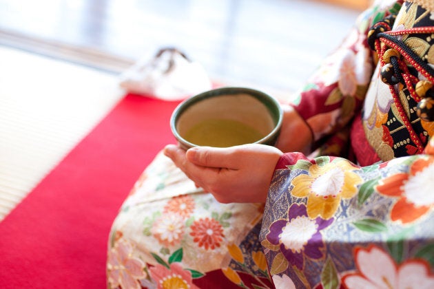 A woman in a Japanese kimono drinking a cup of green tea.