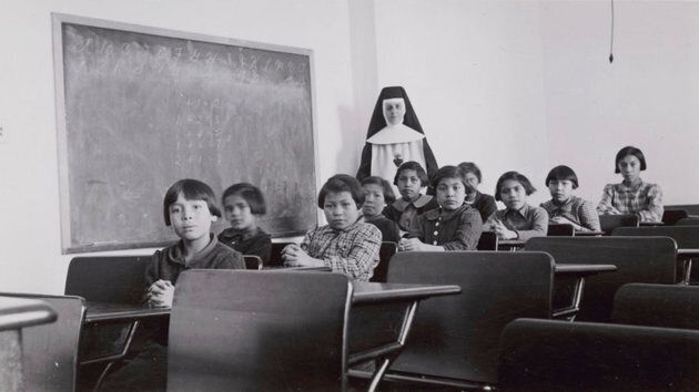 A group of female students and a nun pose in a classroom at Cross Lake Indian Residential School in Cross Lake, Manitoba in a February 1940 archive photo.
