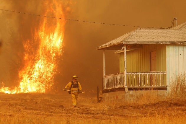 A firefighter walks near a home as flames from the fast-moving Detwiler fire approach in Mariposa, California, U.S. July 19, 2017.