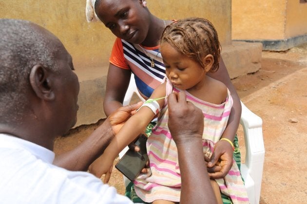 A health worker measures the arm of Hawa Kaba, 3, as her mother, Isatu Kaba, looks on.