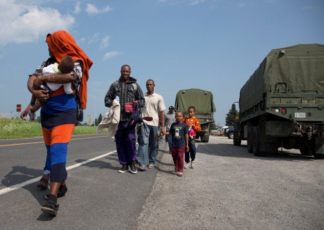 A group of asylum seekers walk down the street as they are escorted from their tent encampment to be processed at Canada Border Services in Lacolle, Quebec, August 11, 2017.