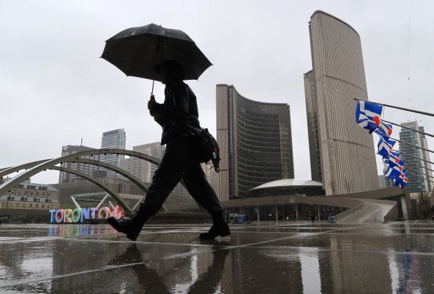 A person walks in the rain through Nathan Phillips Square in front of City Hall in Toronto, Ont.