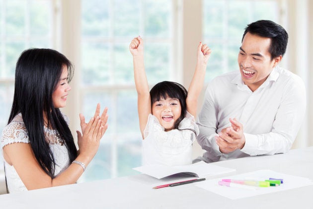 Image of a little girl finishing homework and get applause from her parents at home