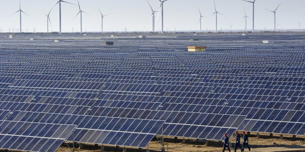 Workers walk past solar panels and wind turbines (rear) at a newly-built power plant in Hami, Xinjiang Uighur Autonomous Region, China, Sept. 17, 2015.