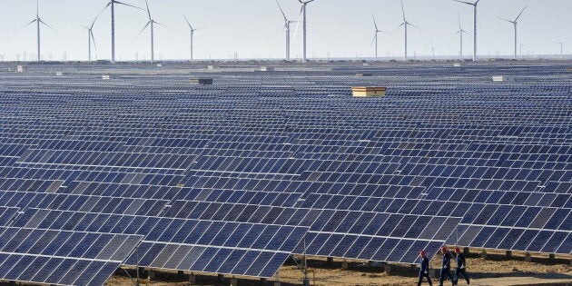 Workers walk past solar panels and wind turbines (rear) at a newly-built power plant in Hami, Xinjiang Uighur Autonomous Region, China, Sept. 17, 2015.