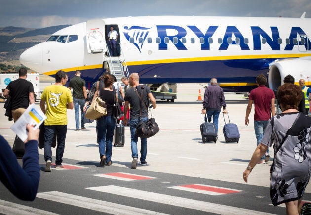 Passengers on the tarmac at Comiso Airport in Sicily, Italy walking with carry-on luggage toward a Ryanair airplane.