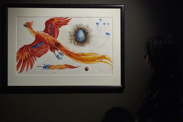 An exhibition curator stands next to an illustration of Fawkes the Phoenix during a preview of 'Harry Potter: A History of Magic' exhibition at the British Library, in central London on October 18, 2017, marking the twentieth anniversary of the publication of Harry Potter and the Philosopher's Stone.