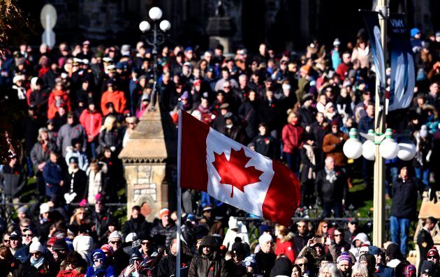 A Canadian flag flies as people line up along Wellington Street and outside Parliament Hill's East Block to watch the National Remembrance Day Ceremony.