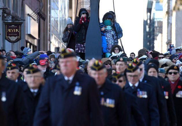 People climb a lamppost to get a better view as veterans march during the National Remembrance Day Ceremony at the National War Memorial in Ottawa.