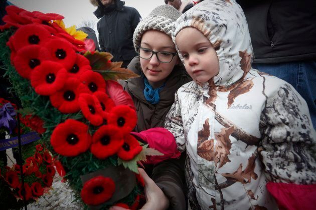 Isolde Chisholm pins her poppy to a wreath with the help of her aunt Rosemund Ragetli at a cenotaph during a Remembrance Day service in Winnipeg.