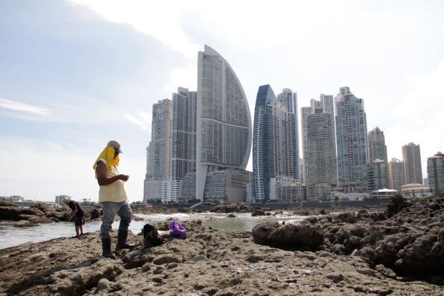 People stand on rocks on the shore during low tide as the Trump Ocean Club International Hotel and Tower Panama (3rd from left) is seen next to apartment buildings in Panama City, Panama October 11, 2017.