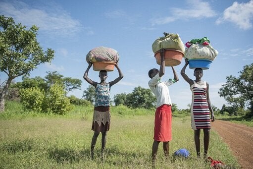 School-age girls in South Sudan carry heavy loads of washing to the river. Their household responsibilities impact their ability to attend school.