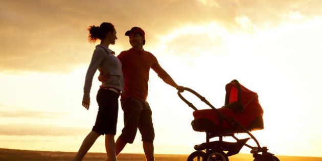 Silhouettes of happy parents walking with stroller on the seacoast