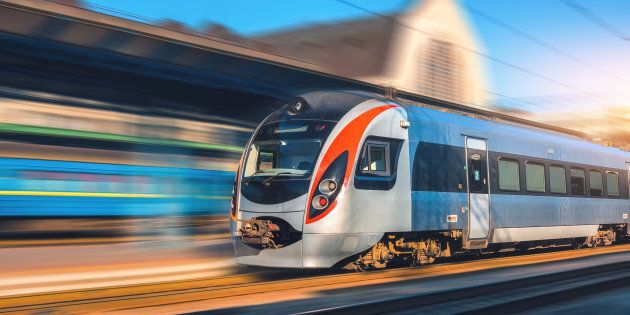 Speed train in motion at the railway station at sunset in Europe. Modern intercity train on the railway platform with motion blur effect. Industrial scene with moving passenger train on railroad