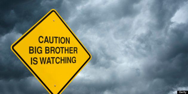 A caution sign in front of storm clouds warning of 'Big Brother is Watching.'