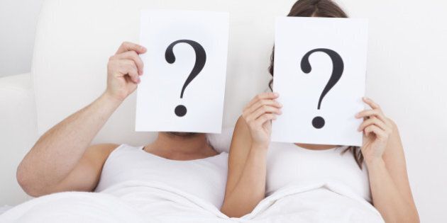 Couple Lying On Bed Holding Question Mark On Face