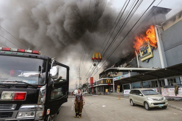 This photo taken on Dec. 23, 2017 shows a firefighter standing in front of a burning shopping mall in Davao City on the southern Philippine island of Mindanao.