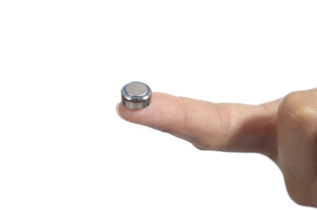 A disc battery compared to the size of a woman's forefinger.