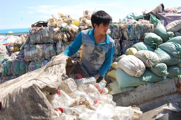 Workers feed the conveyor belt of the bottle grinder at a recycling depot on May 30, 2013, in Laizhou, China. The resulting flakes will be sold to a factory that turns them into fibre suitable for the manufacture of clothes, carpets and other textiles.