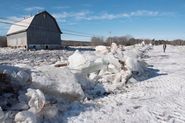 A barn sits surrounded by water and ice as Verona Watson walks between the piles of ice on Route 101 in Hoyt, N.B., on Jan. 14, 2018.
