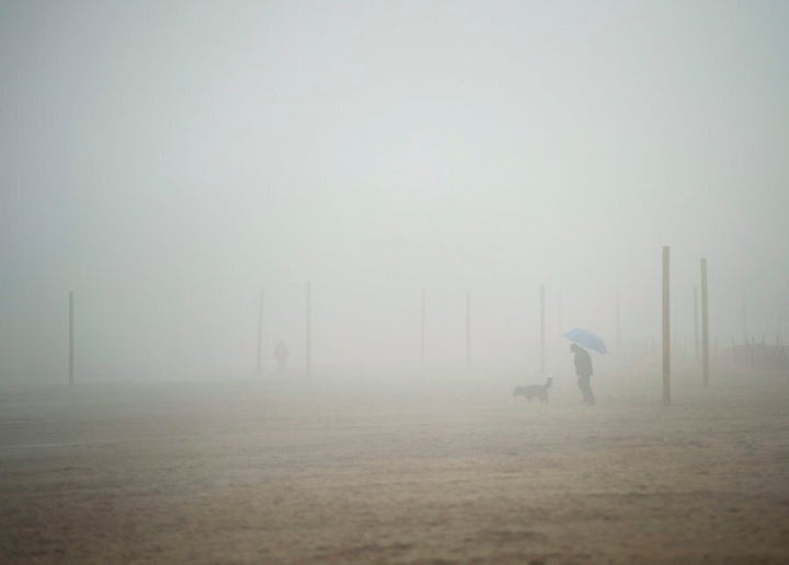 A man walks his dog on the beach during a foggy rainy day in Toronto on March 10, 2016.