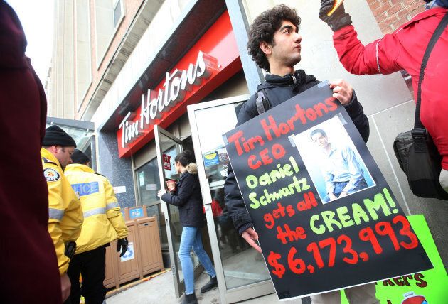 Protesters hold signs outside the Tim Horton's Bloor Street West location, Jan. 10. The rallies were held in response to some Tim Hortons franchisees cutting back paid breaks and benefits in the wake of Ontario's minimum wage hike.