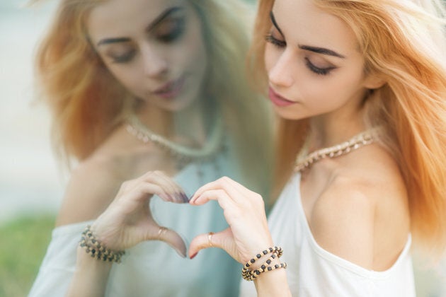 Young beautiful woman making a heart shape by hands in the mirror. Selective soft focus on hand.