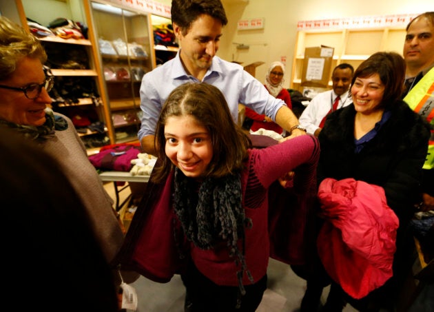 Prime Minister Justin Trudeau helps a young Syrian refugee try on a winter coat after she arrived with her family from Beirut at the Toronto Pearson International Airport in Mississauga, Ont., on Dec. 11, 2015.