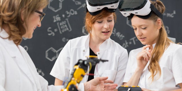 Shot of two students wearing virtual reality glasses and working in a classroom with their teacher