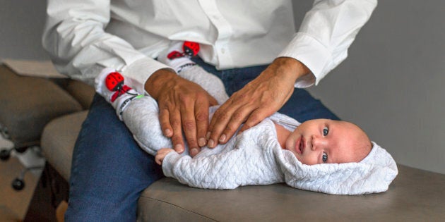 A chiropractor adjusts a one-month-old baby.