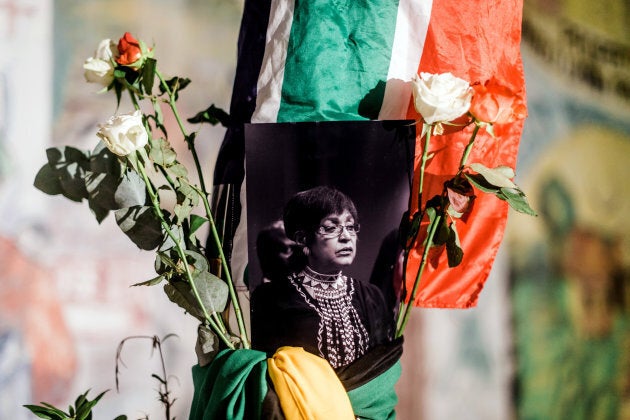 A black and white photograph of the late Winnie Madikizela-Mandela is surrounded by South African and African National Congress flags on a pole at the Old Durban Prison's Human Rights wall as South Africans gather to pay respect to the late activist during a candle vigil in Durban on April 2, 2018.