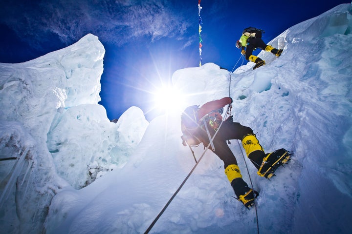 Two climbers scaling a vertical cliff in the Khumbu Icefall