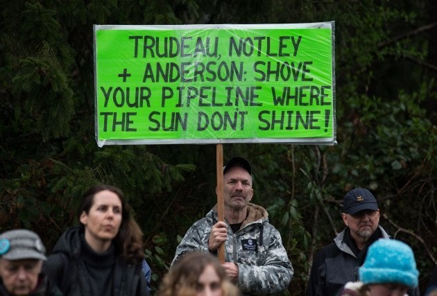 A man holds a sign while listening as other protesters opposed to the Kinder Morgan Trans Mountain pipeline extension defy a court order and block an entrance to the company's property, in Burnaby, B.C., on April 7, 2018.