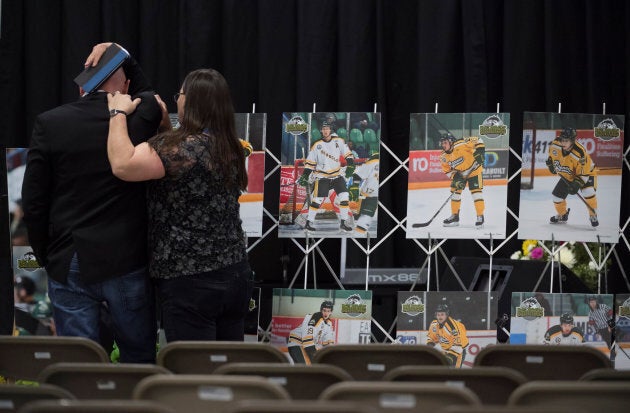 A man is comforted as he looks at photographs before a vigil at the Elgar Petersen Arena, home of the Humboldt Broncos, to honour the victims of a fatal bus accident in Humboldt, Sask. on April 8, 2018.