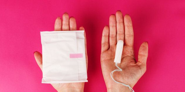Woman holding menstrual tampon and pad on a pink background. Menstruation time. Hygiene and protection.