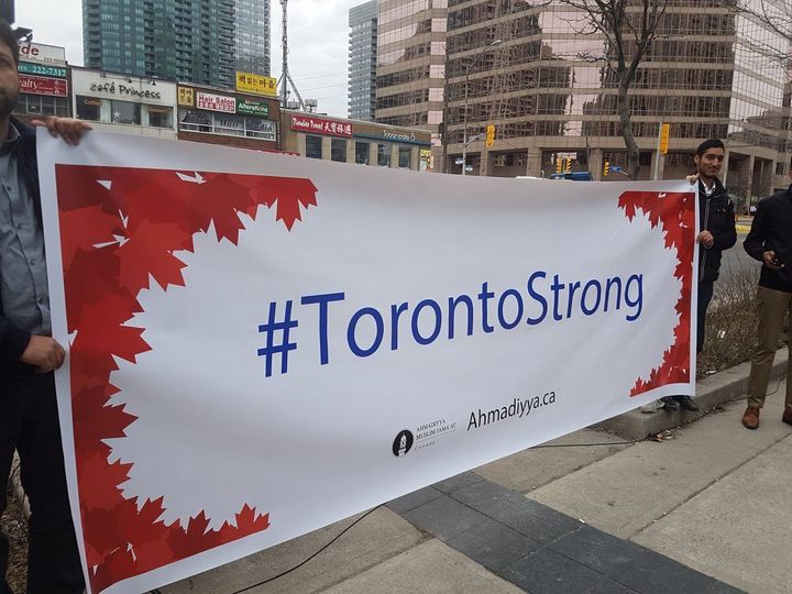 A banner from Ahmadiyya Muslim Jama'at Canada is held up at a memorial at Yonge Street near Finch Avenue for victims of the Toronto van attack.