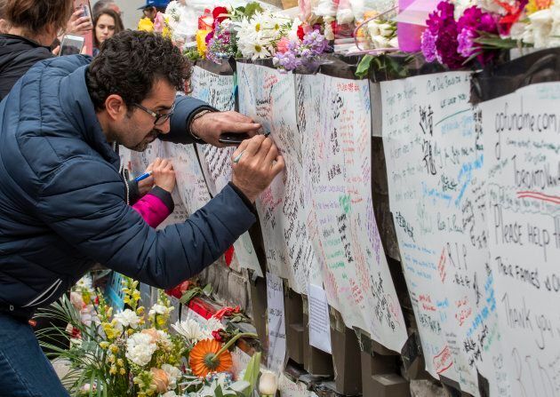 A man writes a message at a makeshift memorial across the street from where a man in a rented van plowed into pedestrians on Yonge Street in northern Toronto.