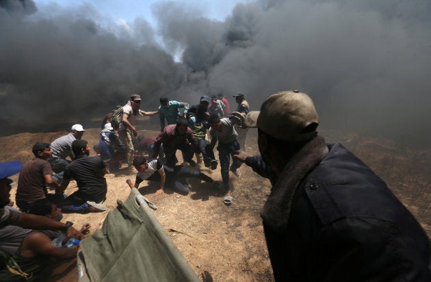 A wounded Palestinian demonstrator is evacuated as others take cover from Israeli fire and tear gas during a protest against U.S. embassy move to Jerusalem and ahead of the 70th anniversary of Nakba, at the Israel-Gaza border in the southern Gaza Strip on May 14, 2018.