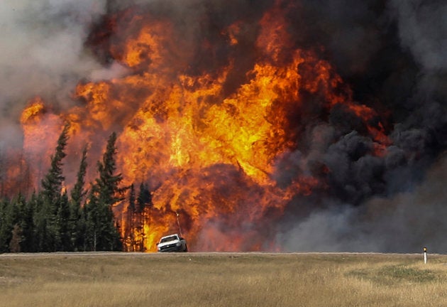 Smoke and flames from the wildfires erupt behind a car on the highway near Fort McMurray, Alta. on May 7, 2016.