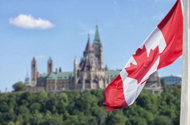 Canadian flag waving with Parliament Buildings hill and Library in the background.