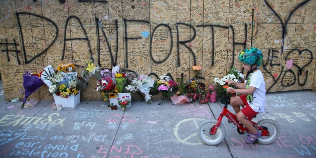 A boy passes messages written on construction boarding after a mass shooting on Danforth Avenue in Toronto on July 25, 2018.