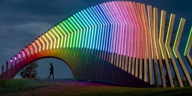 A man walks under Moving Surfaces, a giant steel and light sculpture at Ottawa's Lansdowne Park, as it is lit up in the colours of the rainbow, during Pride Week on Saturday.