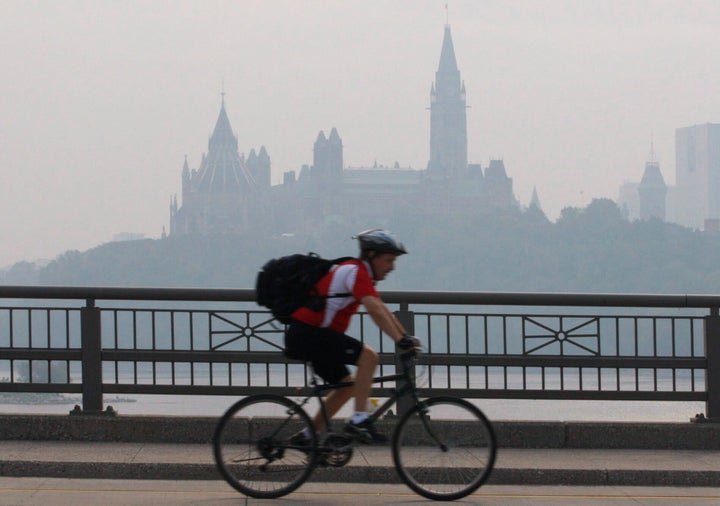 A cyclist make his way across a bridge into Ottawa as the Parliament buildings are seen through haze in Ottawa, Canada on May 31, 2010.