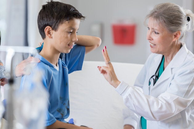 Senior female emergency room doctor holds up two fingers to young injured soccer player.