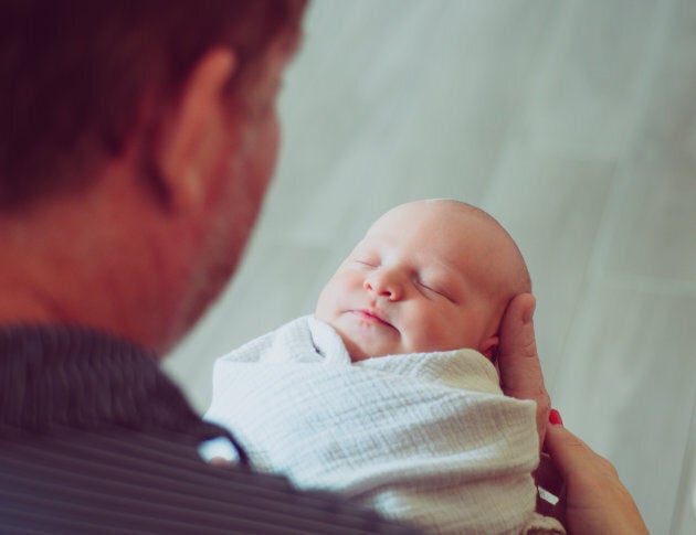 Adorable newborn, swaddled up and full of the cutest baby wrinkles, being held by dad at home in a candid, classic pose. Mother and father look at their beautiful sleeping newborn together. heartwarming moment. Home interior, life events and parenthood