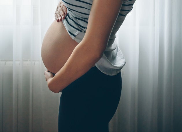 Side View Of Pregnant Woman Standing By Window At Home