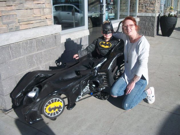 Troy poses with his barber Katie, proudly showing off the custom Batmobile costume that fits over his wheelchair.
